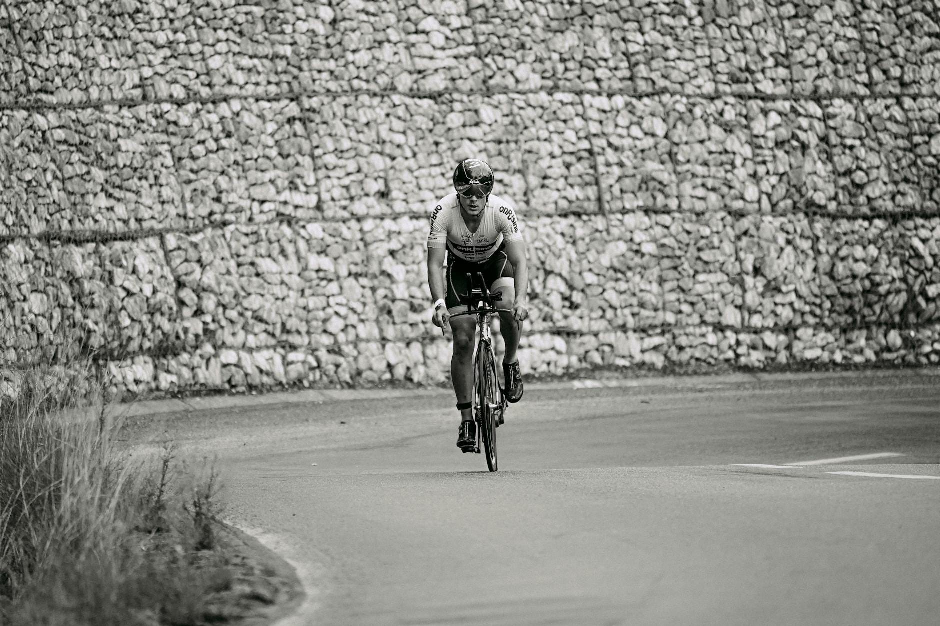 Kolarz w stroju sportowym jedzie szosą wzdłuż kamiennego muru