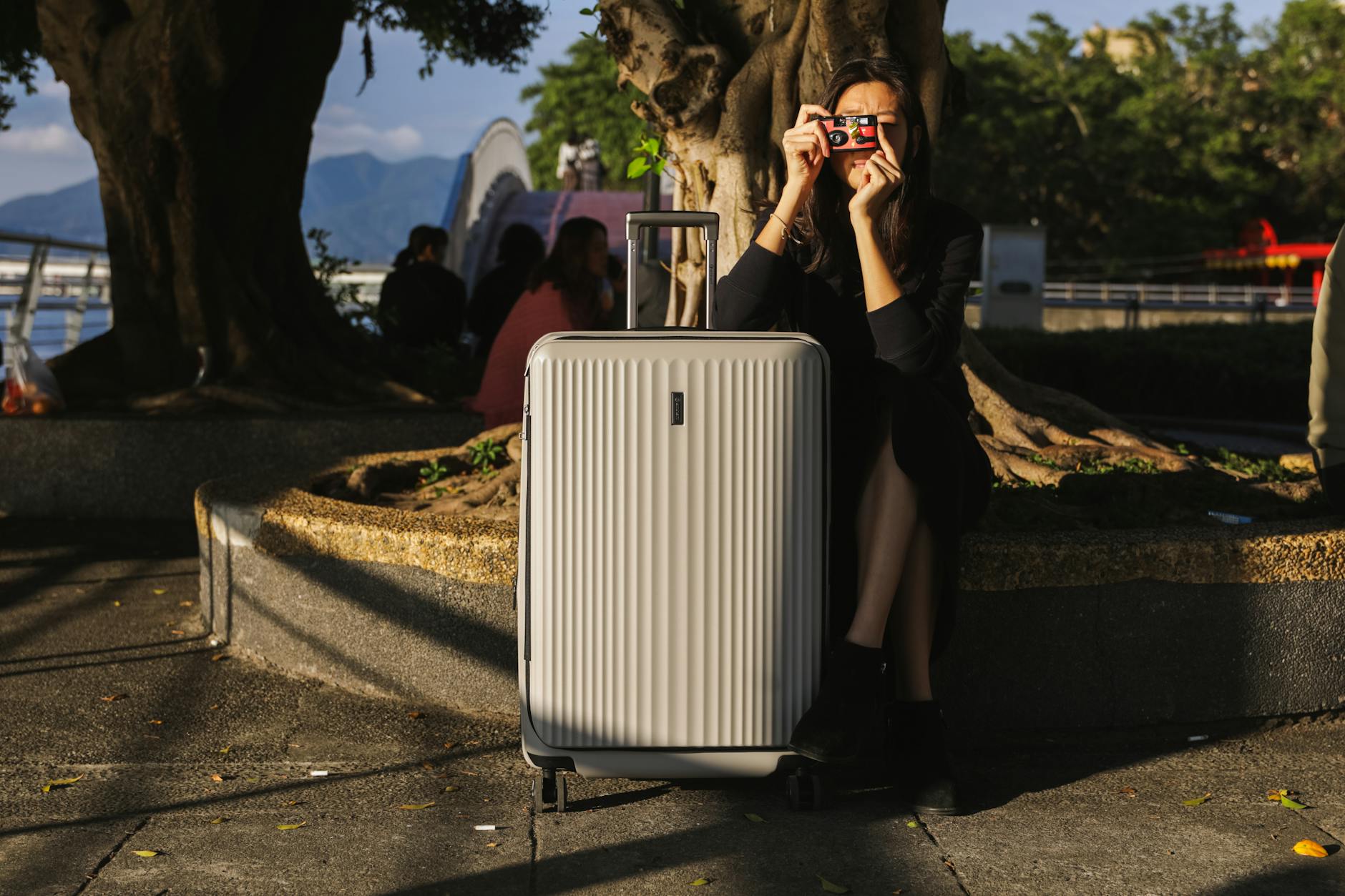 Kobieta z walizką i aparatem fotograficznym spaceruje po miejskim parku